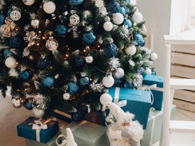 Stock photo of beautiful decorated Christmas tree with blue and silver and white balls and wrapped Christmas presents under the tree. Two Santa Claus figures under tree.